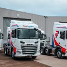 Four Pass Logistics branded 6x2 tractor units parked in two rows in front of a warehouse.