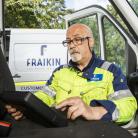 A Fraikin employee in a high-visibility jacket sits inside a vehicle cab, using a digital tablet.
