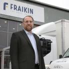 Man wearing glasses, stood in front of two parked vehicles.