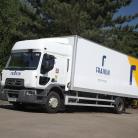 A Fraikin delivery truck is parked on a paved surface, surrounded by lush green trees and a blue sky. The truck bears the Fraikin logo and branding on its side.
