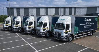 A fleet of five Tremco trucks parked in a row in front of a warehouse.