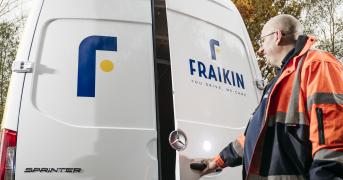 Man in orange high visibility jacket opens the rear door of a white Sprinter van, displaying the Fraikin logo