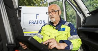 A Fraikin employee in a high-visibility jacket sits inside a vehicle cab, using a digital tablet.