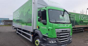 A green and white Fishers laundry service truck parked outdoors. The truck features the company's logo and website, fisherslaundry.co.uk, on its side along with an image of a stag.