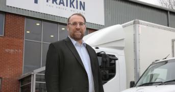 Man wearing glasses, stood in front of two parked vehicles.