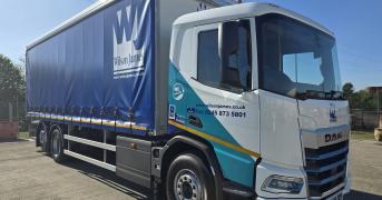 A Wilson James branded DAF XD Electric rigid, parked in a depot on a sunny day