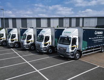 A fleet of five Tremco trucks parked in a row in front of a warehouse.
