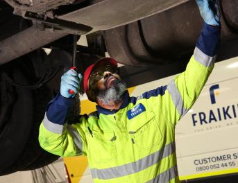 Fraikin mechanic checks under a vehicle raised on a ramp