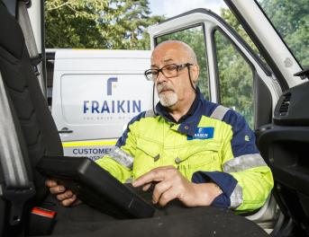 A Fraikin employee in a high-visibility jacket sits inside a vehicle cab, using a digital tablet.
