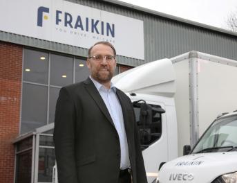 Man wearing glasses, stood in front of two parked vehicles.