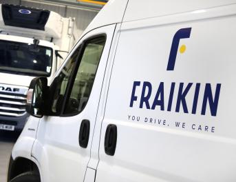 The image shows a white Fraikin van in the foreground with the company logo and slogan "You Drive, We Care" on its side. In the background, there is a DAF truck inside a garage or warehouse setting.