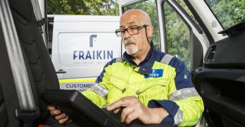 A Fraikin employee in a high-visibility jacket sits inside a vehicle cab, using a digital tablet.