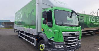 A green and white Fishers laundry service truck parked outdoors. The truck features the company's logo and website, fisherslaundry.co.uk, on its side along with an image of a stag.