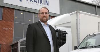 Man wearing glasses, stood in front of two parked vehicles.