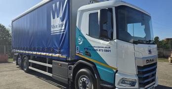 A Wilson James branded DAF XD Electric rigid, parked in a depot on a sunny day